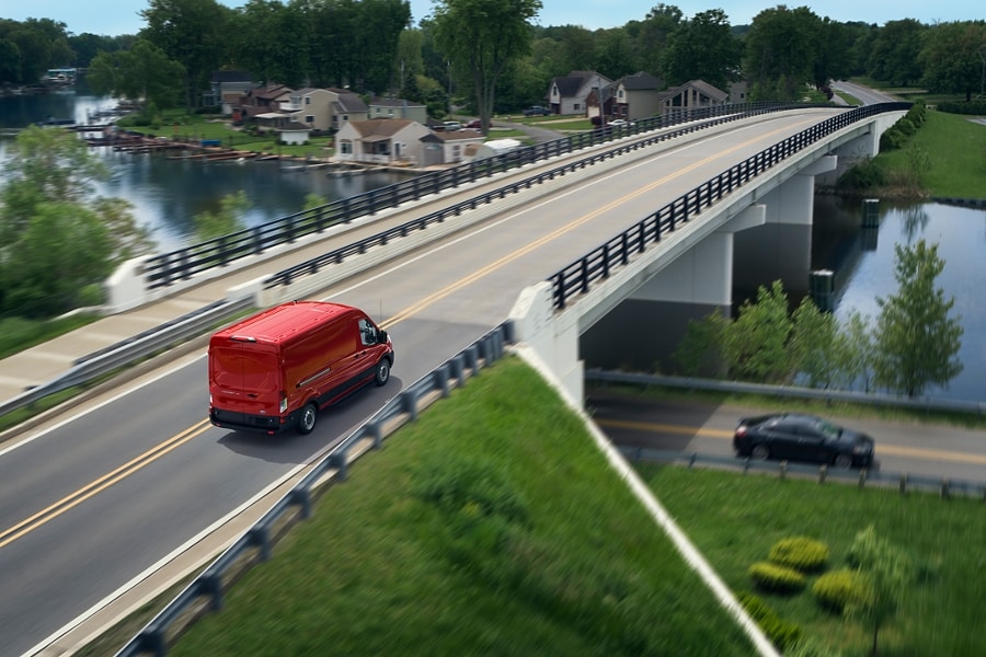 A red Ford E Transit crosses a highway bridge
